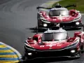 Dos coches de carreras rojos compiten en Le Mans, sus luces brillan en la pista.