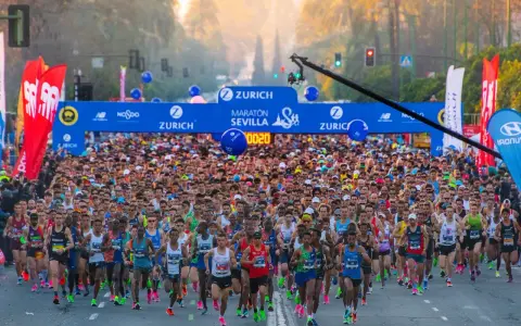 Multitudinaria salida del maratón Sevilla 2026, con miles de corredores bajo el arco de meta.