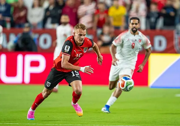 Jugadores de fútbol en acción. El número 15 de Austria corre con el balón, mientras otro jugador se acerca. ¿Quién juega hoy?