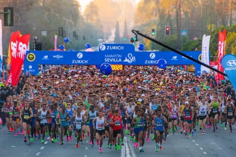 Multitudinaria salida del maratón Sevilla 2026, con miles de corredores bajo el arco de meta.
