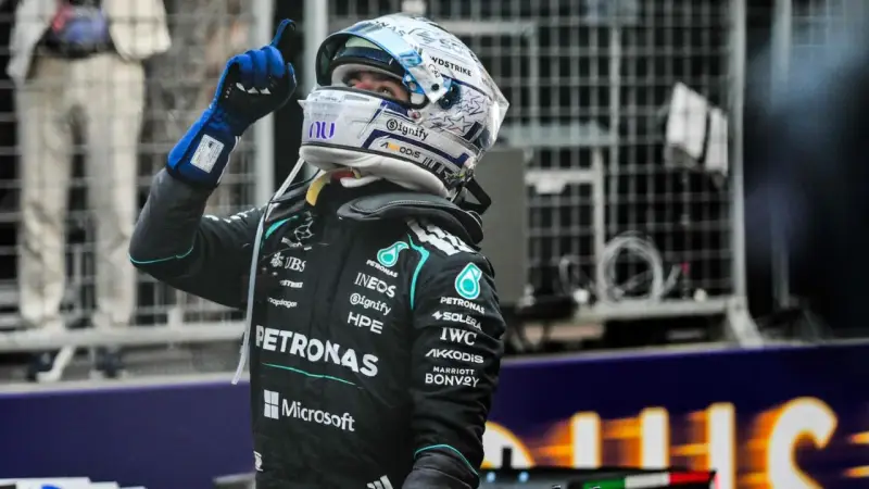 Piloto de F1 con casco y guantes azules levanta el dedo índice, celebrando una victoria en la carrera F1 Mónaco.