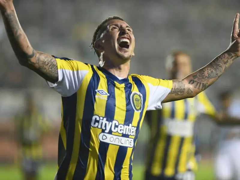 Jugador de Rosario Central celebra un gol, con los brazos en alto y la boca abierta. Sus tatuajes son visibles en sus brazos.